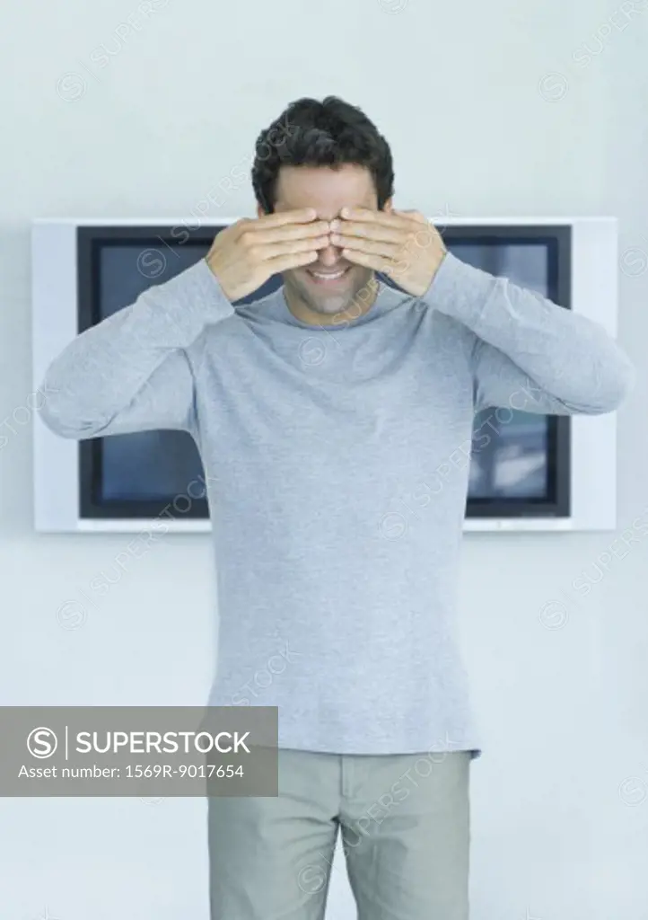 Man standing in front of widescreen TV on wall, hands covering eyes