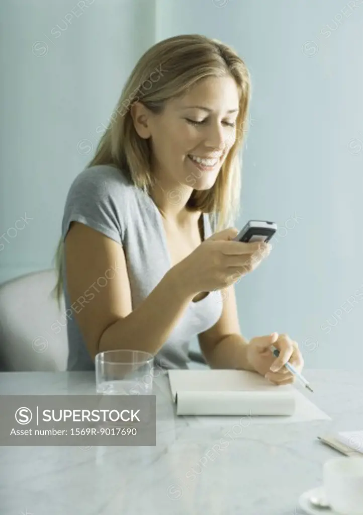 Woman sitting at table, looking at cell phone, smiling