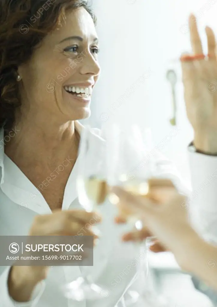 Mature professional woman smiling, holding up keys, clinking champagne glasses with unseen person