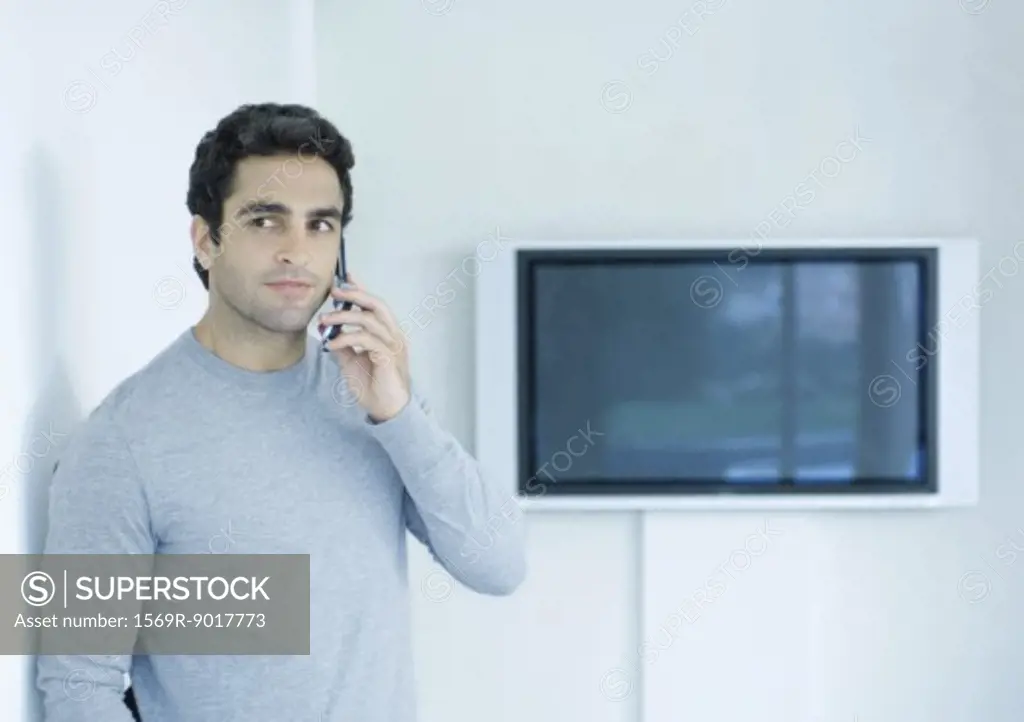 Man using cell phone, widescreen TV in background