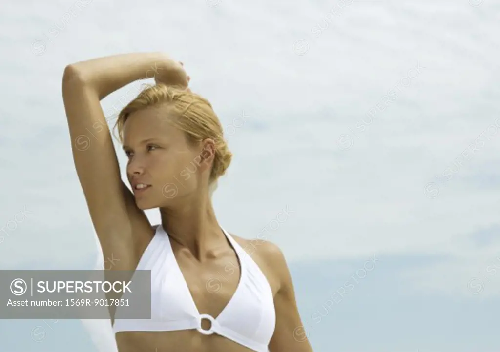 Woman in bikini standing with arm up, looking away