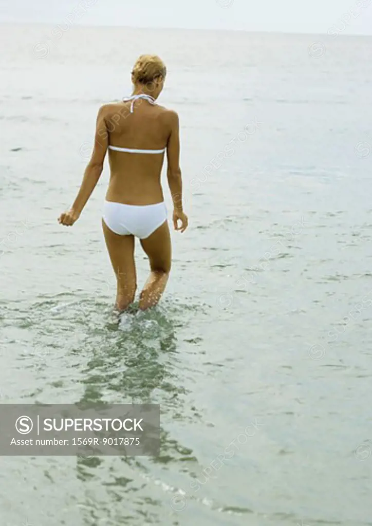 Woman in bikini, knee deep in water, rear view