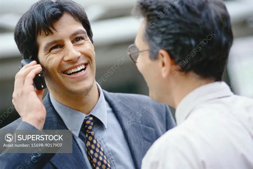Businessman using phone, colleague facing him, head and shoulders