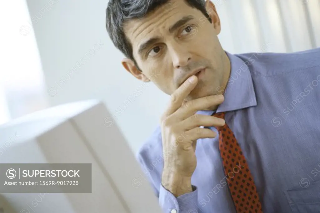 Businessman sitting at computer, finger at lip, looking away