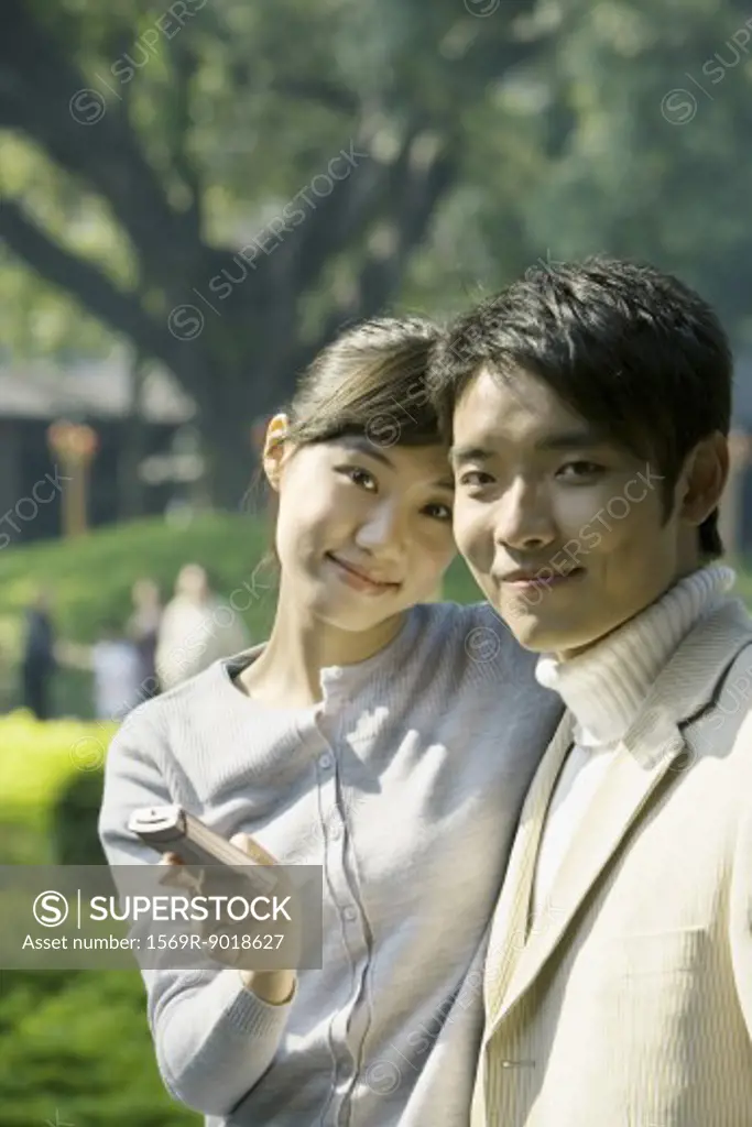 Young couple with cell phone, smiling at camera, portrait