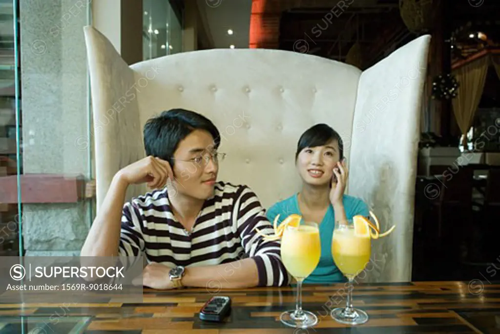 Young couple sitting in booth, woman using cell phone