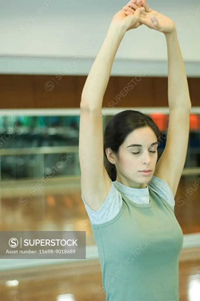 Young woman stretching arms overhead, eyes closed