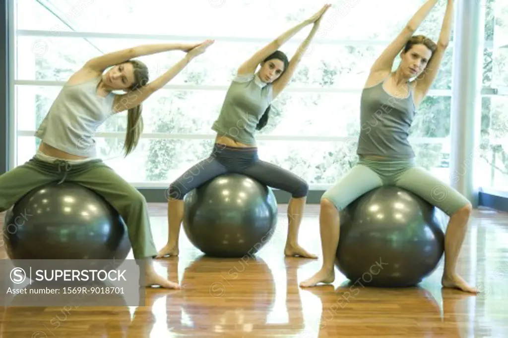 Young women sitting on fitness balls, doing side stretch