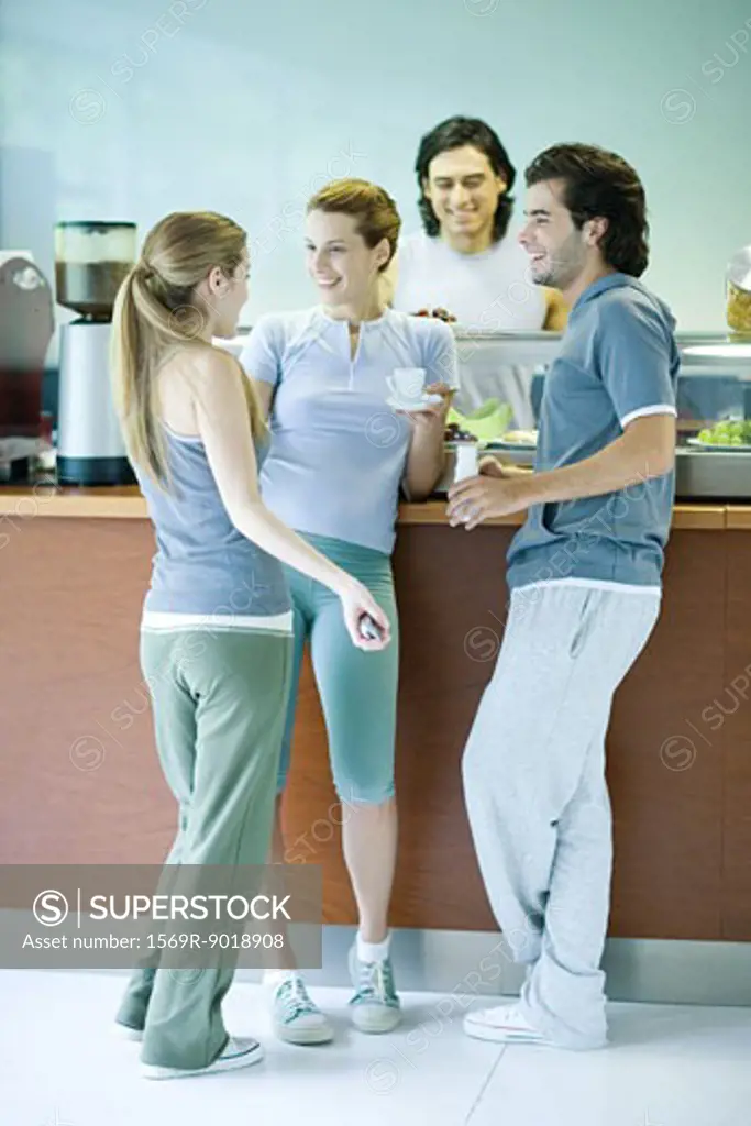 Young adults dressed in exercise clothes, standing by snack bar, chatting