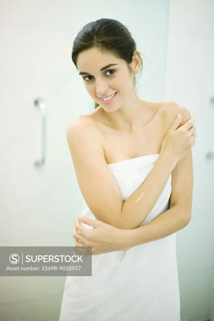 Woman standing wrapped in towel, hand on shoulder, looking at camera