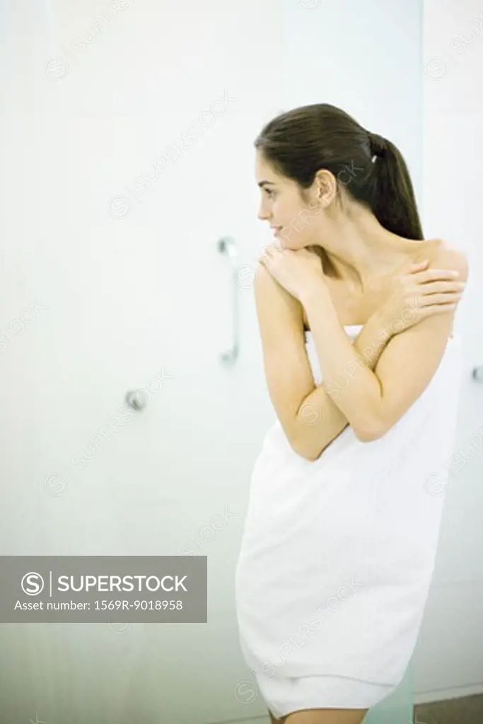 Woman standing wrapped in towel, hands on shoulders, looking away
