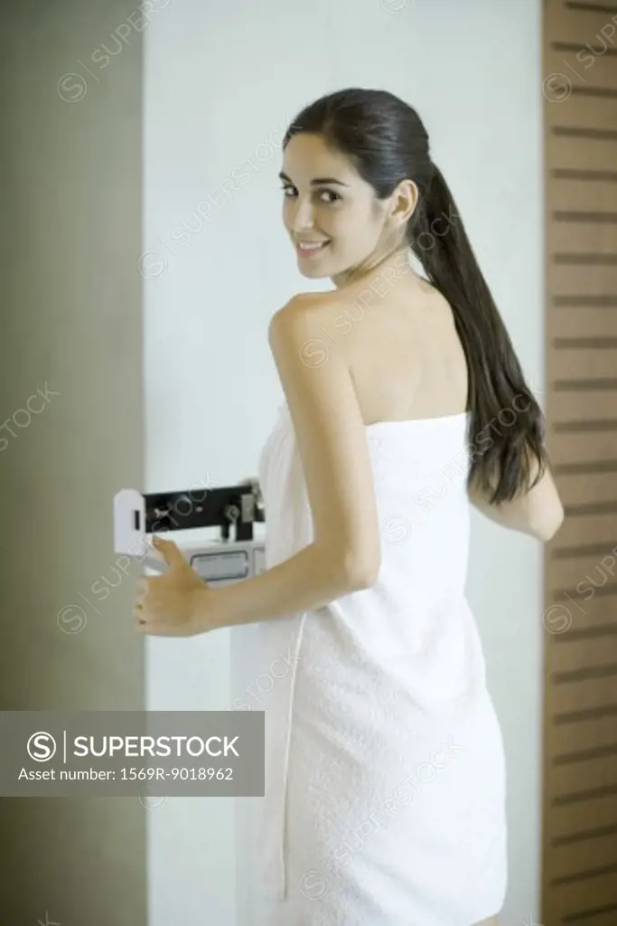 Woman wrapped in towel, standing on scale, looking at camera