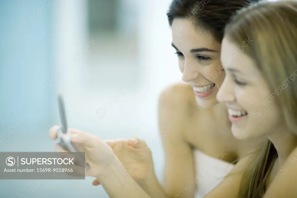 Two women wrapped in towels, looking at cell phone together, close-up