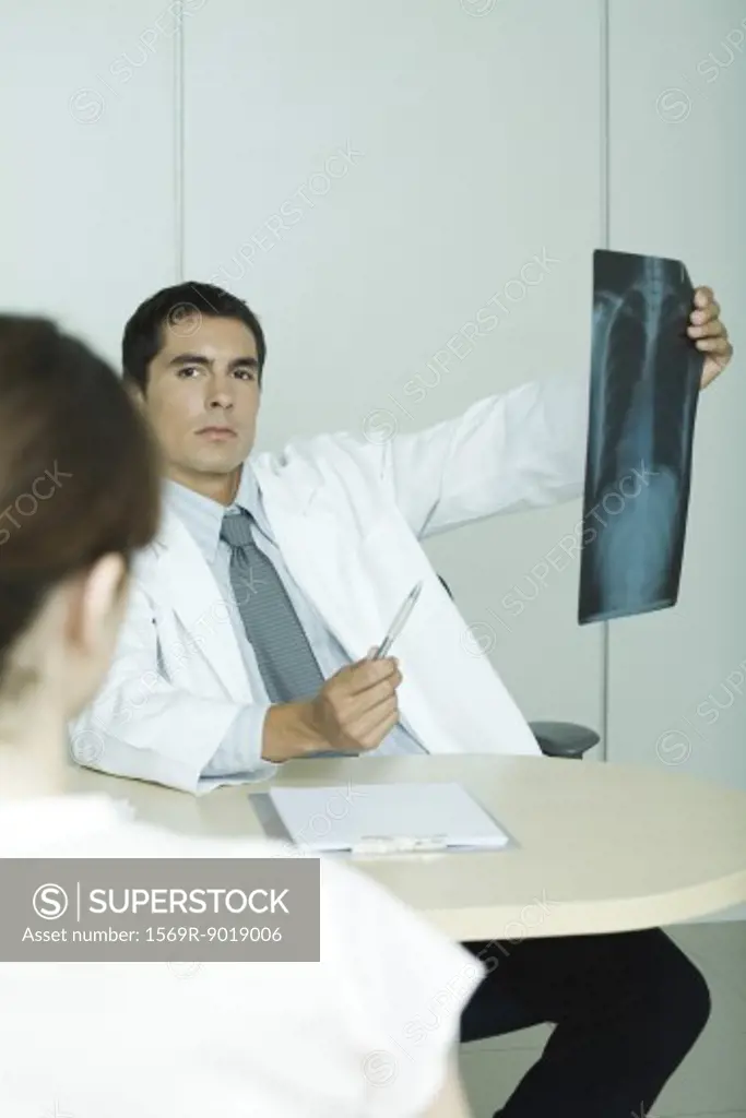 Doctor sitting across from female patient, holding up x-ray