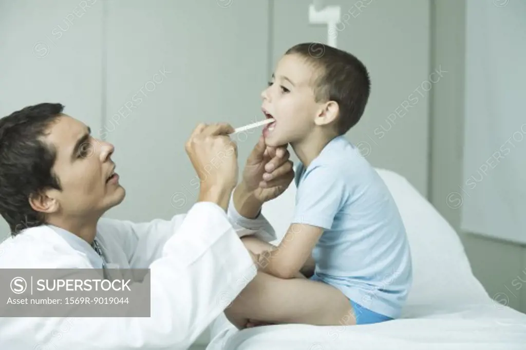 Doctor holding down boy's tongue with tongue depressor
