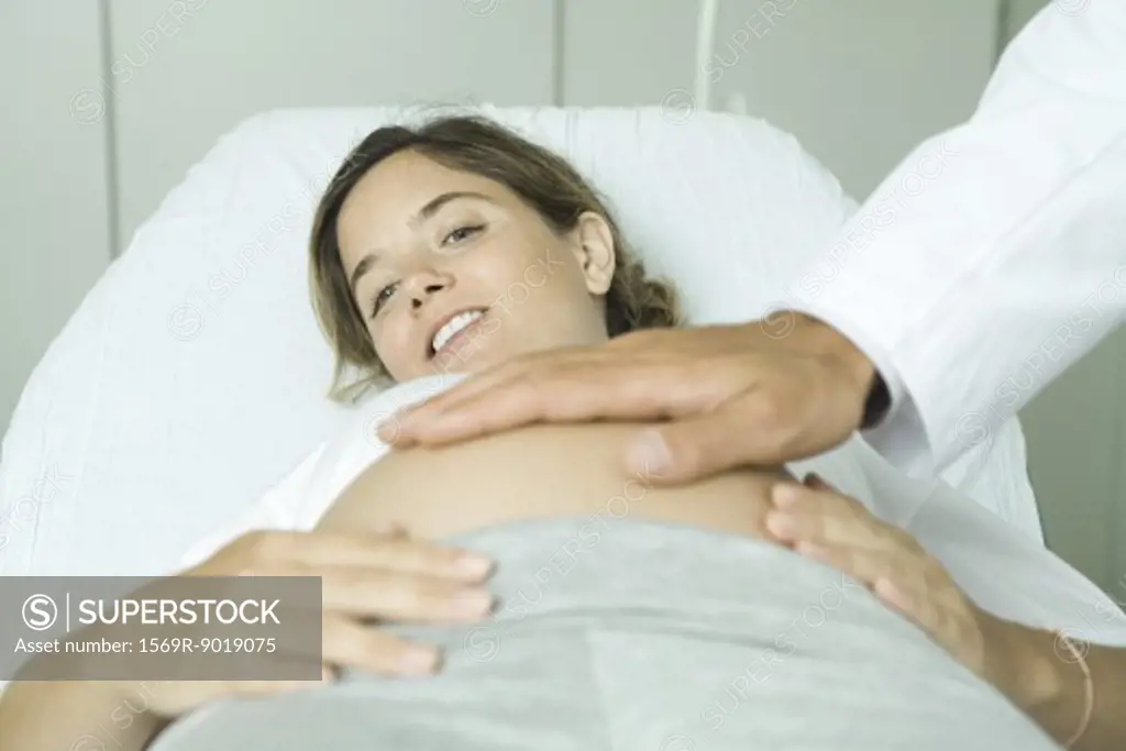Pregnant woman lying on back, doctor's hand on stomach