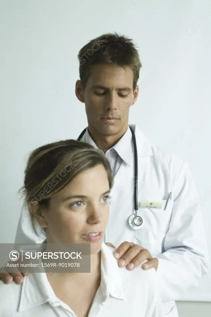 Doctor standing behind woman, hands on her shoulders