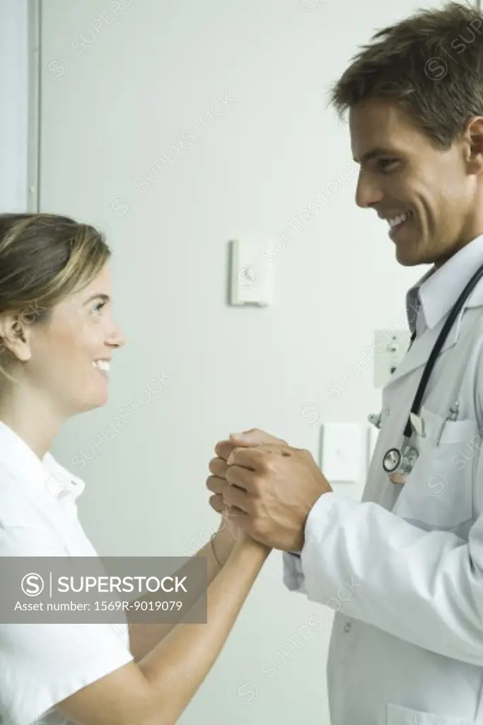 Doctor and woman standing face to face, holding hands and smiling at each other