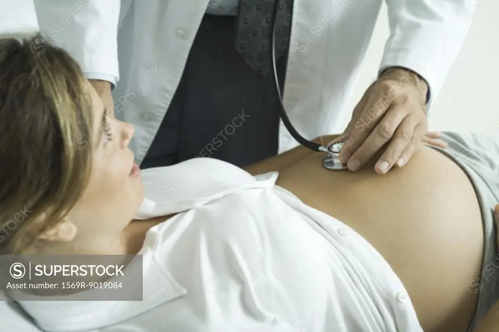 Doctor listening to pregnant woman's stomach with stethoscope