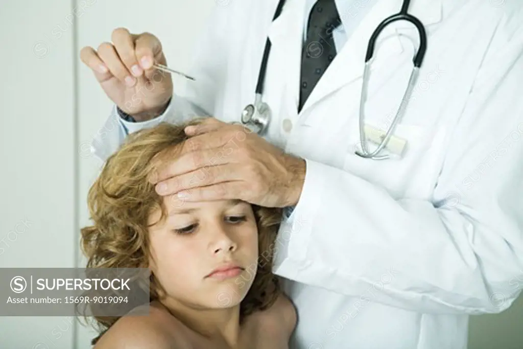 Doctor feeling boy's forehead and holding thermometer