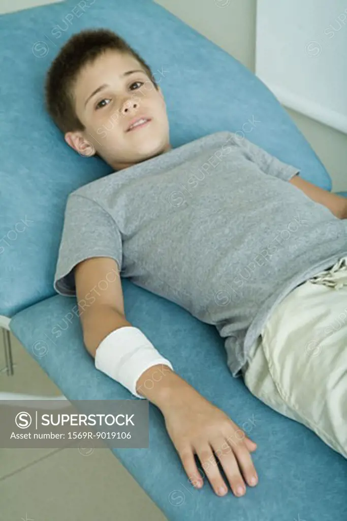 Boy lying on examination table with bandage around arm