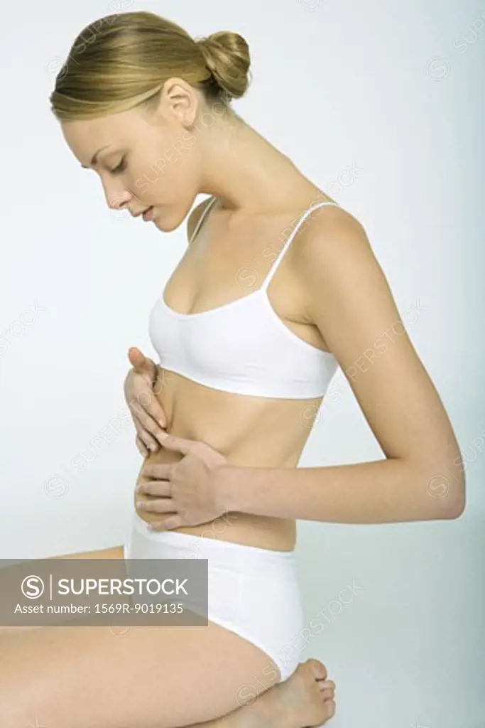 Woman sitting in underclothes, touching abdomen