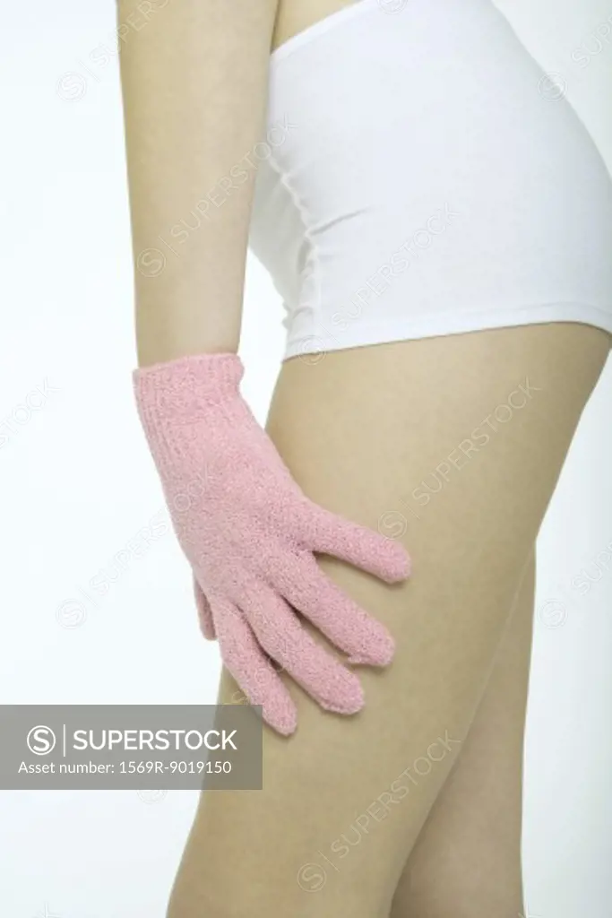 Young woman touching leg with massage glove, close-up of mid-section