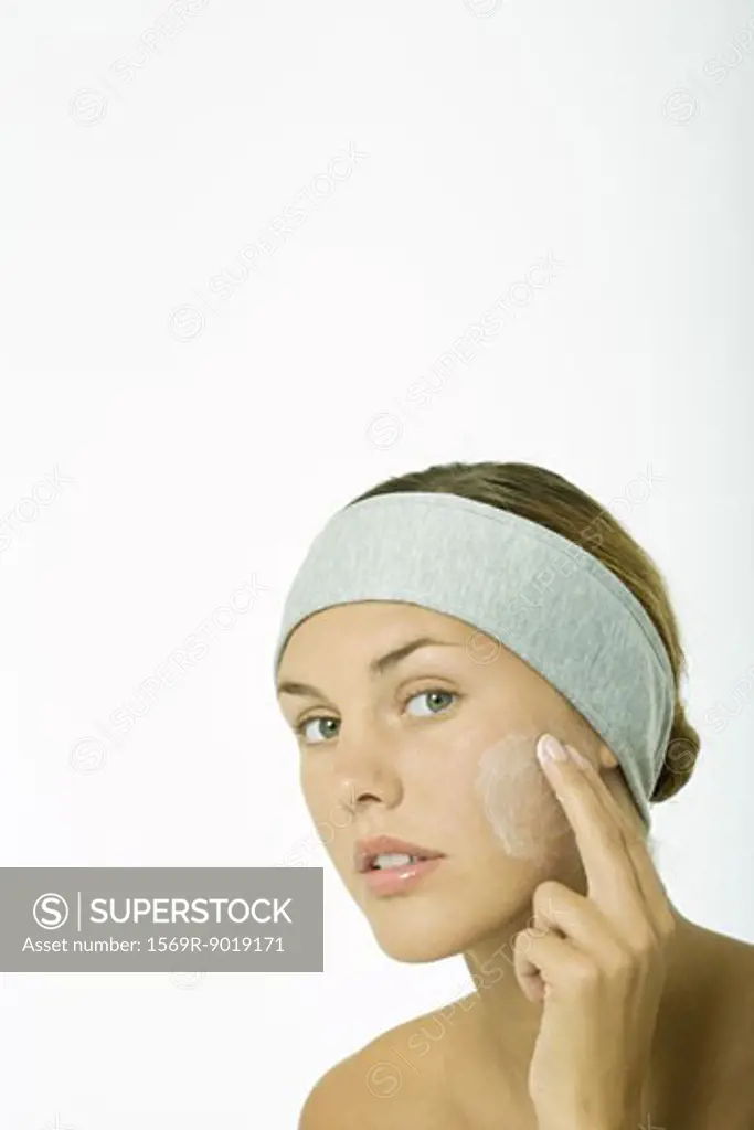 Young woman applying facial cleanser to cheek, head and shoulders