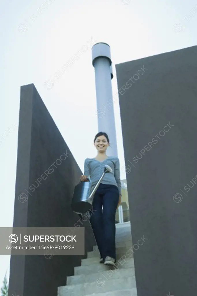 Young woman walking down stairs, carrying watering can