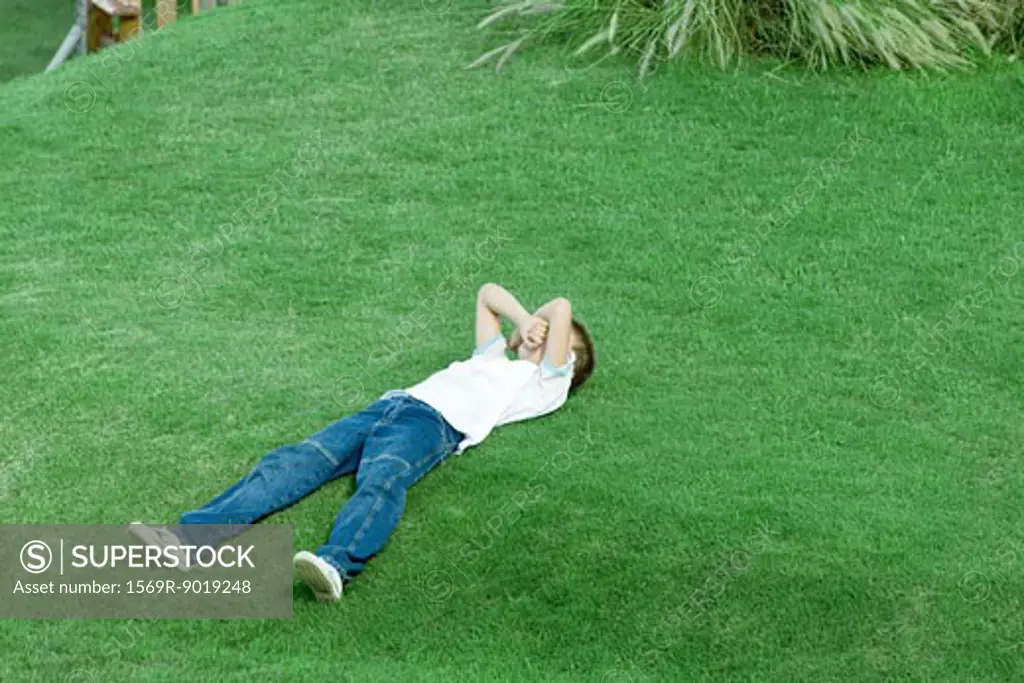 Boy lying on grass, covering face with arms, full length