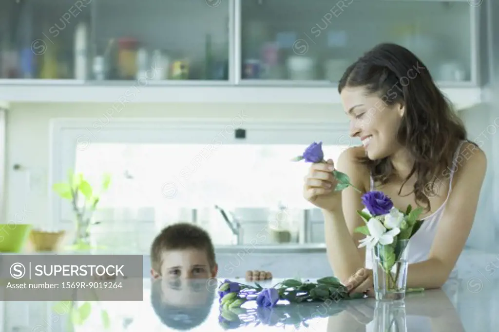 Young woman making fresh flower arrangement, smiling at boy