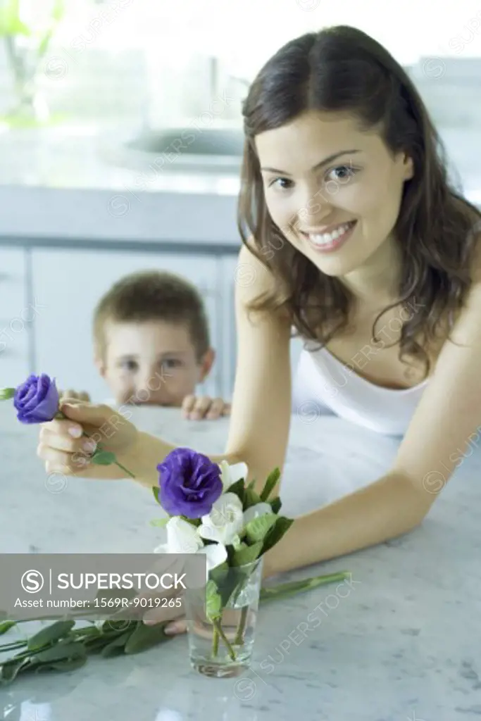 Young woman making fresh flower arrangement, next to boy, smiling