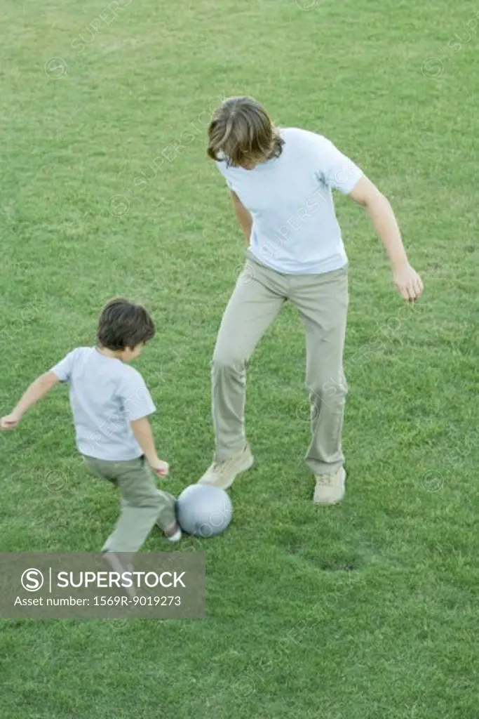 Young man and boy playing soccer on lawn, high angle view