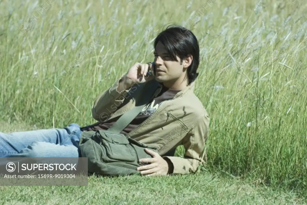Man lying in grass, using cell phone