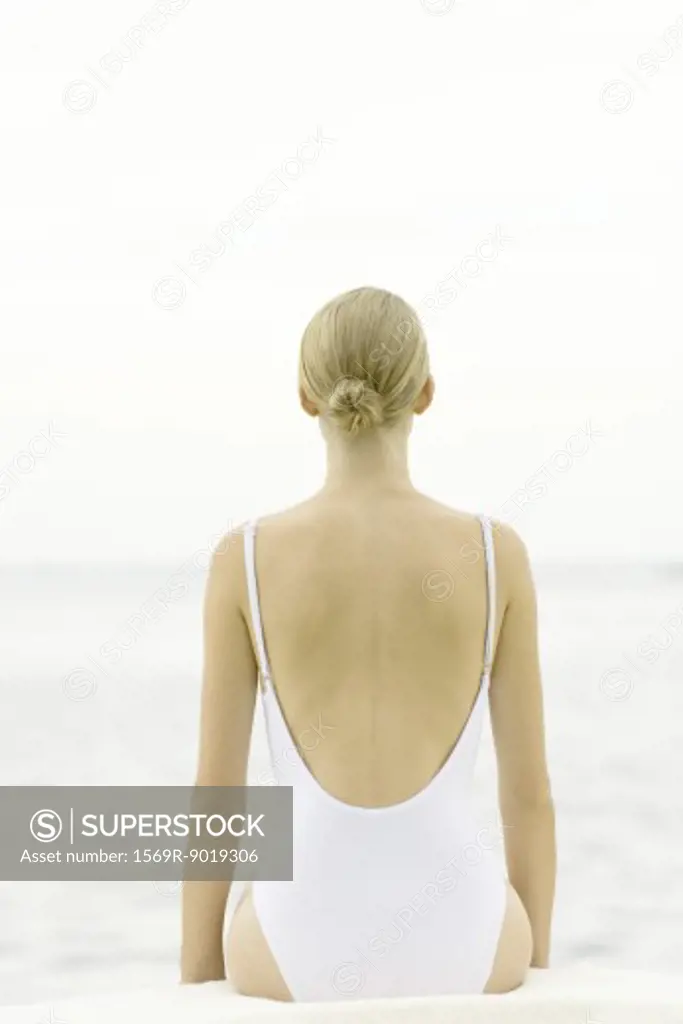 Teenage girl sitting on beach, rear view