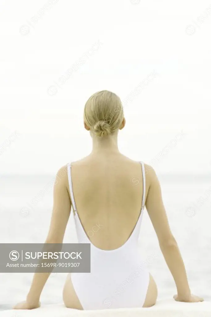 Teenage girl sitting, wearing bathing suit, rear view