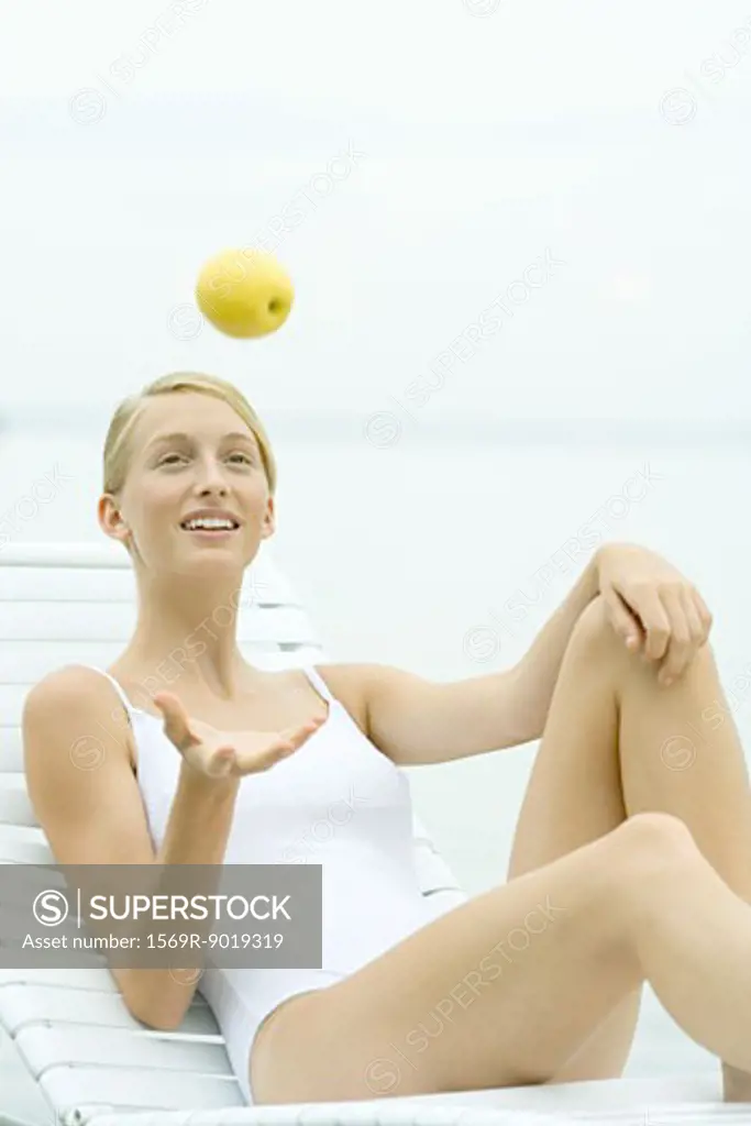Teenage girl wearing bathing suit, tossing apple into air