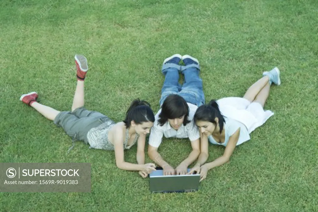 Young friends lying in grass, using laptop together