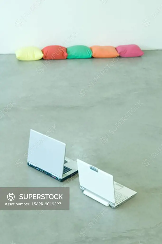 Two laptops on floor, cushions in background