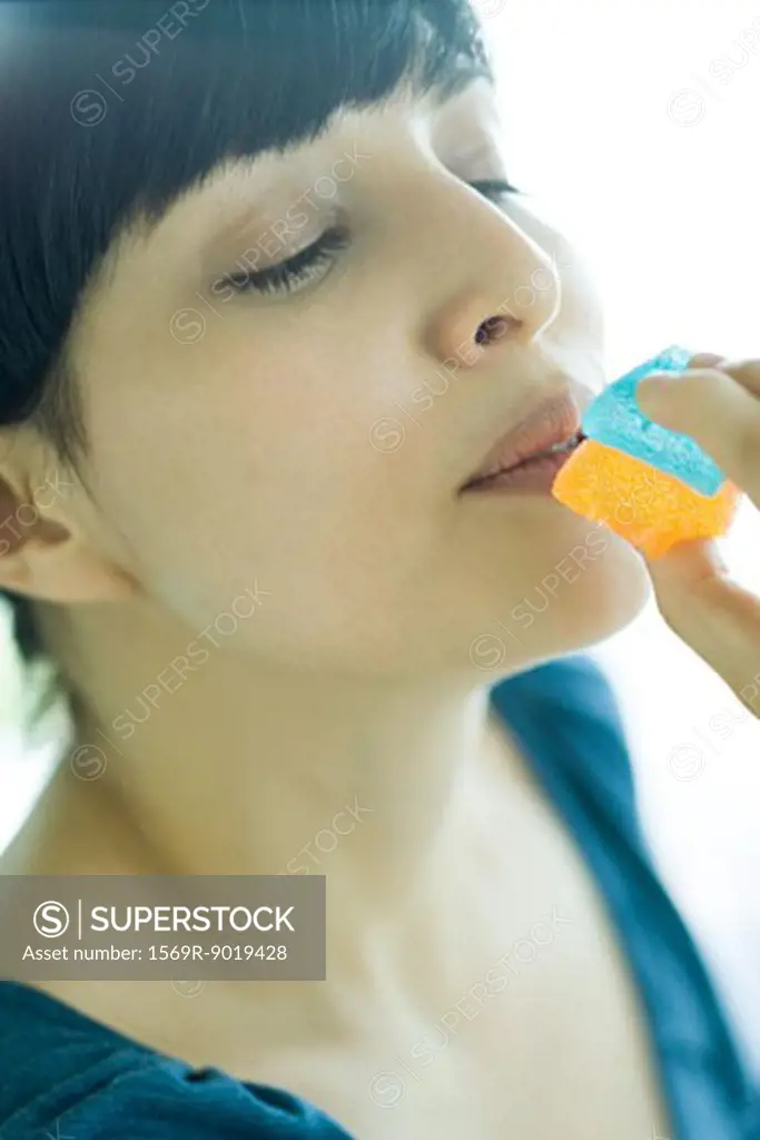 Woman holding up piece of candy to mouth, eyes half-closed