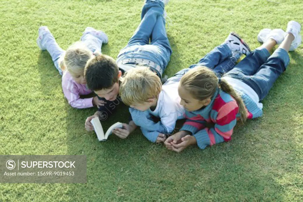 Children lying on grass together, reading