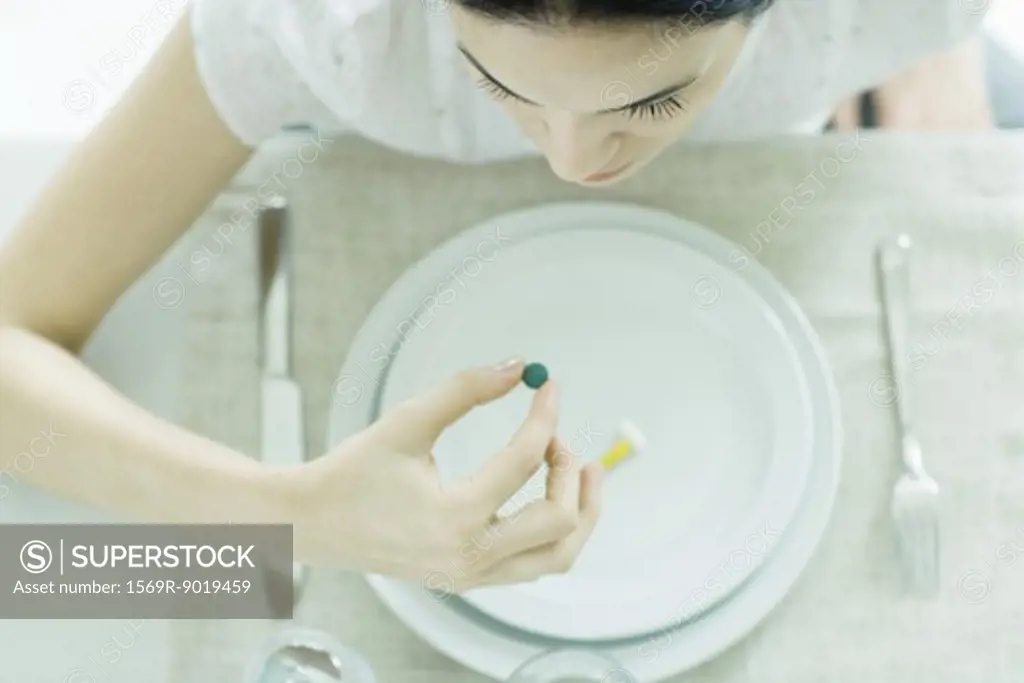 Woman sitting at empty plate holding vitamin
