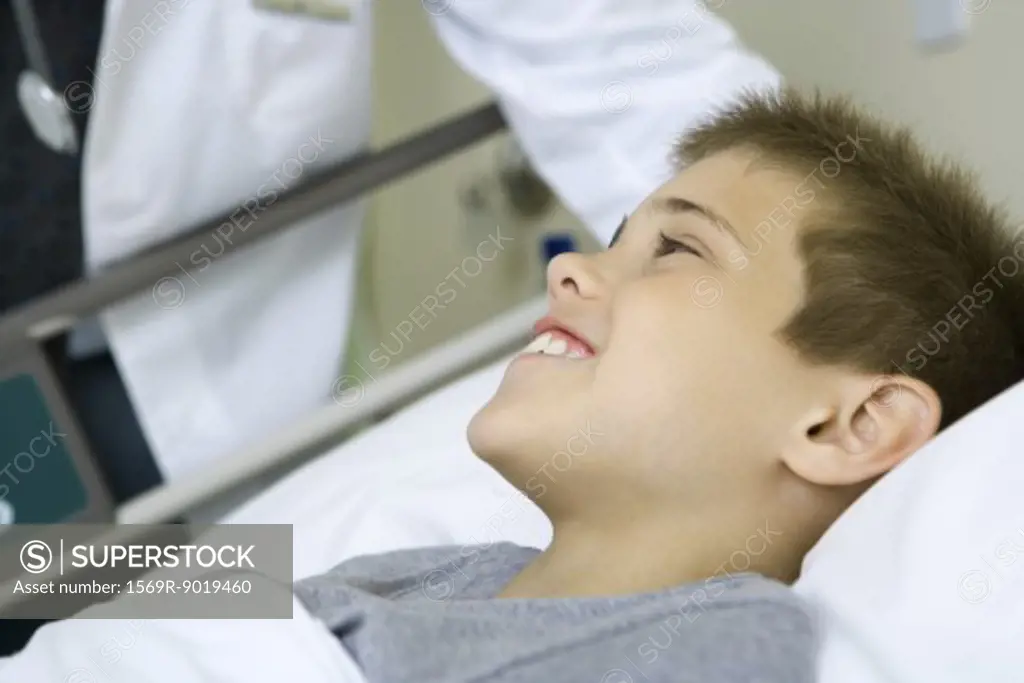 Child lying in hospital bed, doctor standing by side
