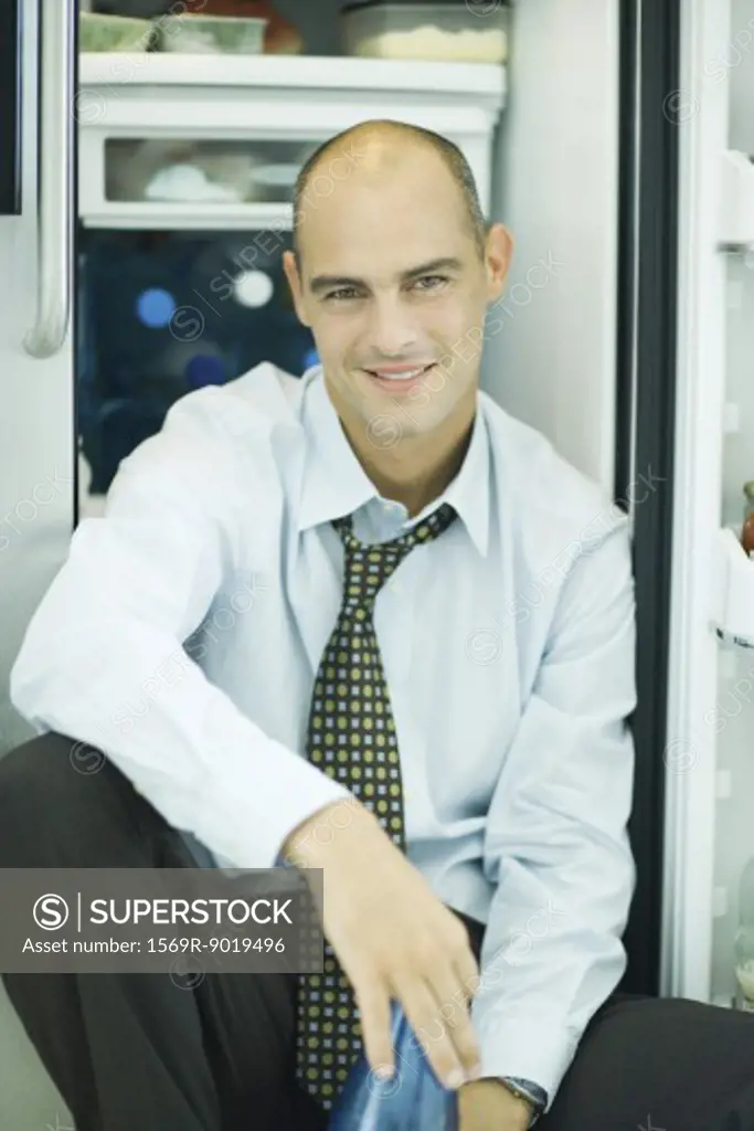 Man sitting in front of open refrigerator, smiling at camera