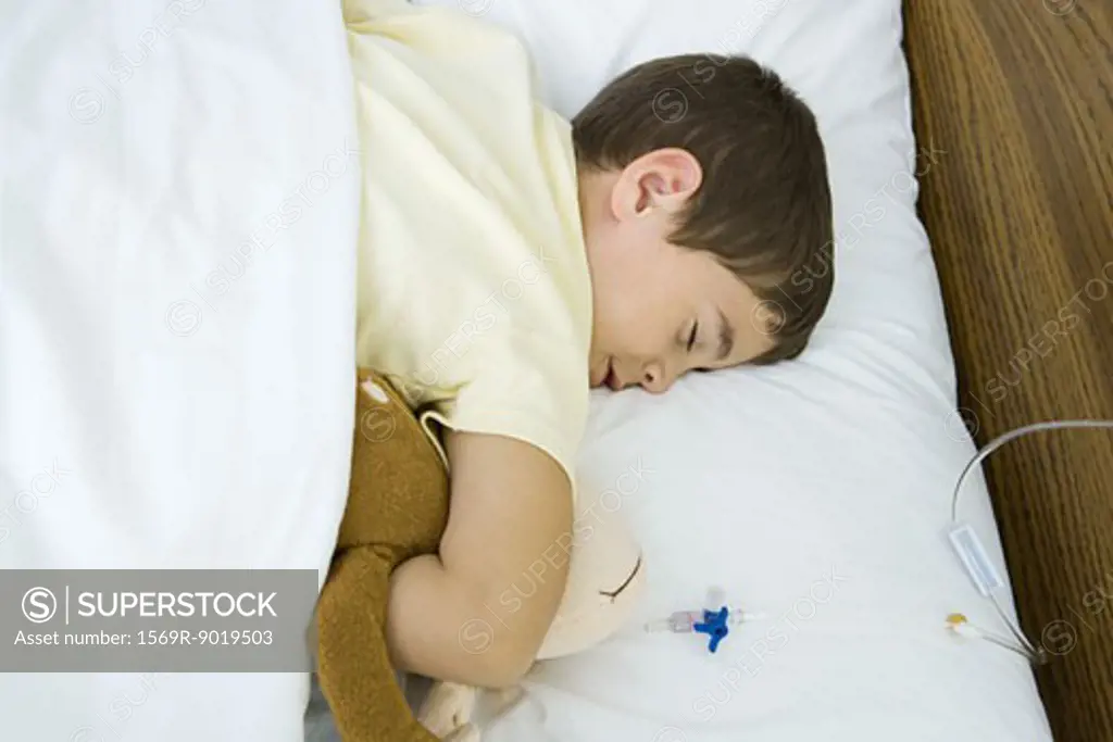 Boy lying in hospital bed, holding stuffed animal