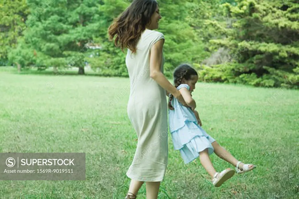 Woman swinging little girl around on grass