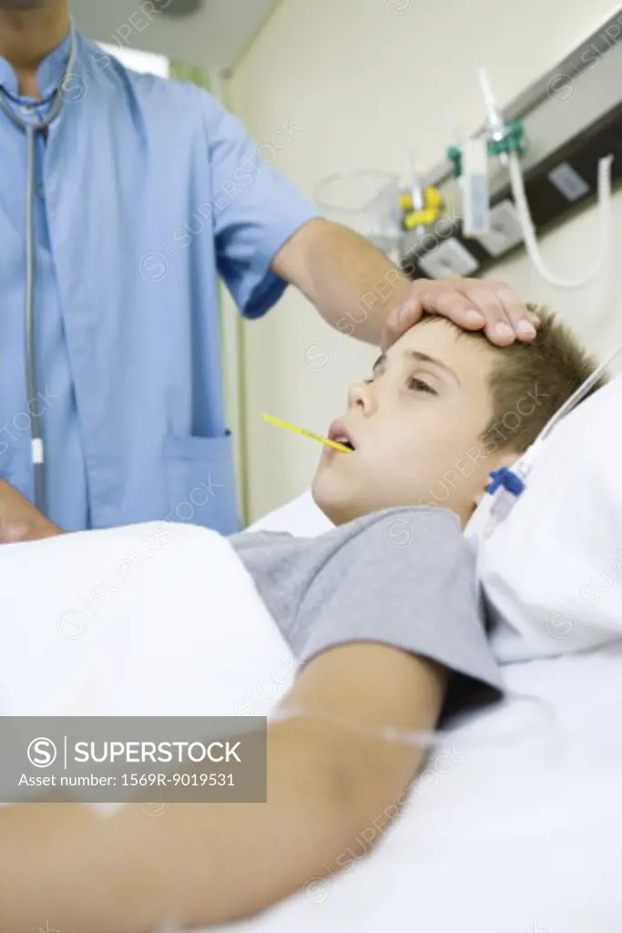 Boy lying in hospital bed, doctor taking temperature and feeling forehead