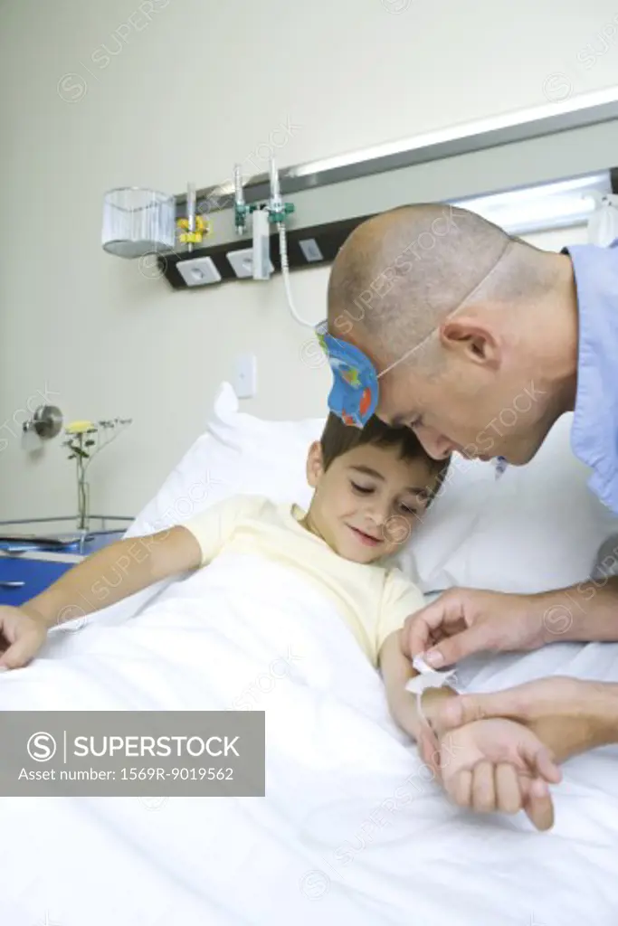 Boy lying in hospital bed, nurse adjusting IV