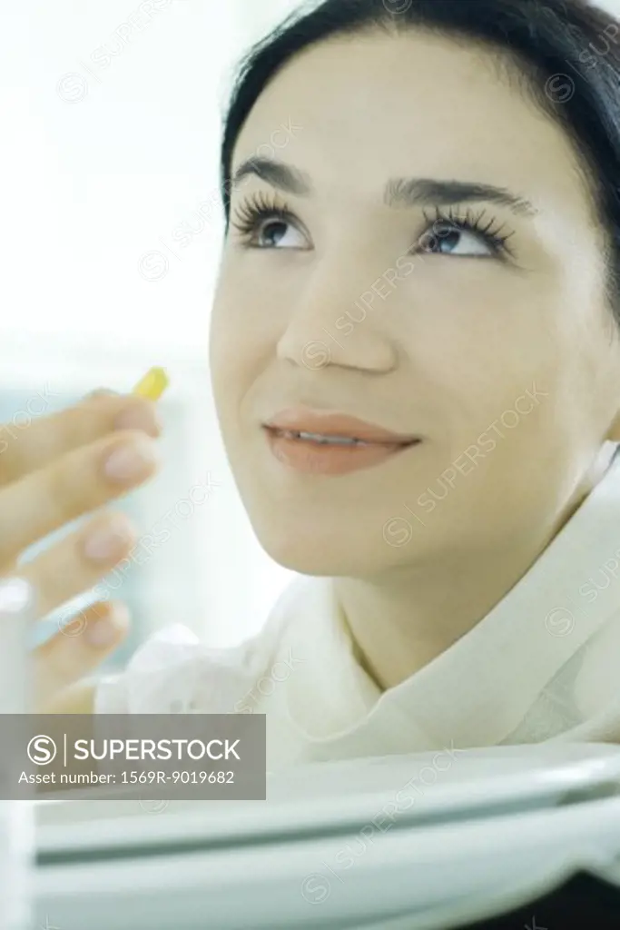 Woman holding up vitamin, looking up