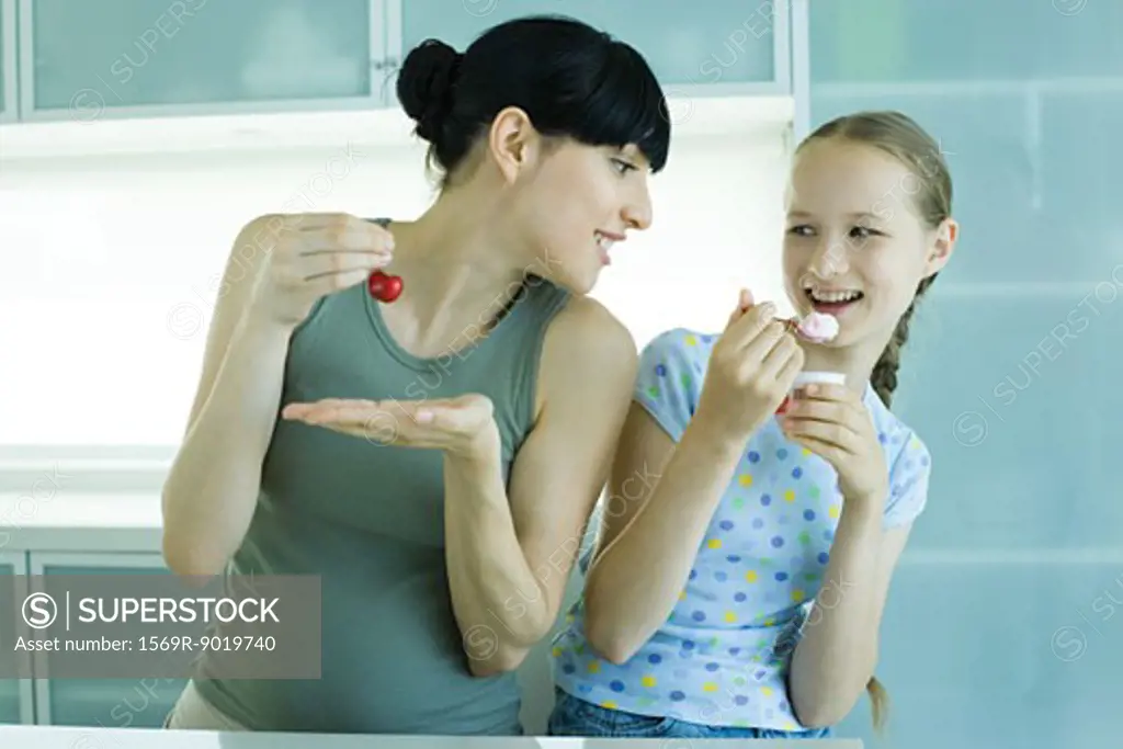 Girl holding ice cream dessert, next to woman holding cherry, woman leaning toward girl